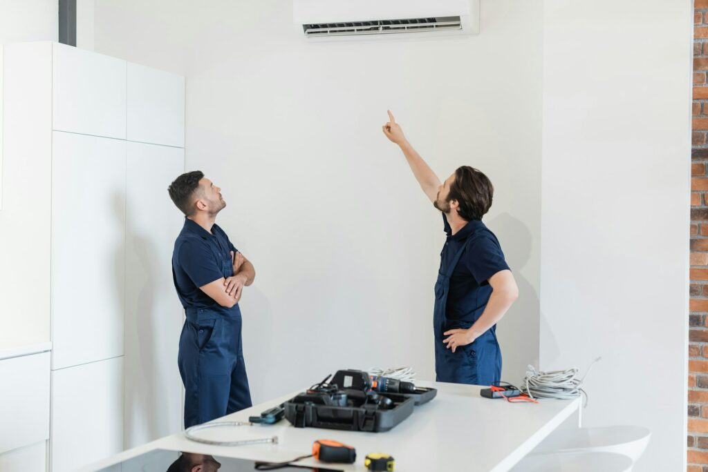 repairman pointing at air conditioner near colleague and tool on kitchen table